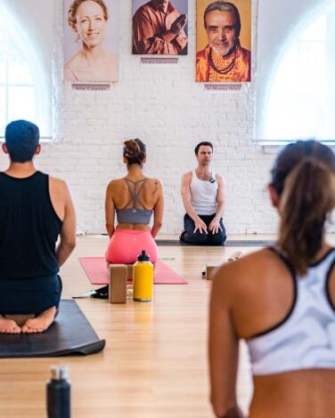 Yoga class with students practicing seated meditation in a bright studio.