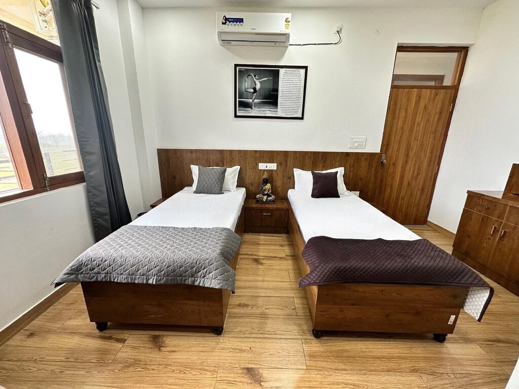 Simple bedroom with two single beds, wooden furniture, and a window with curtains.