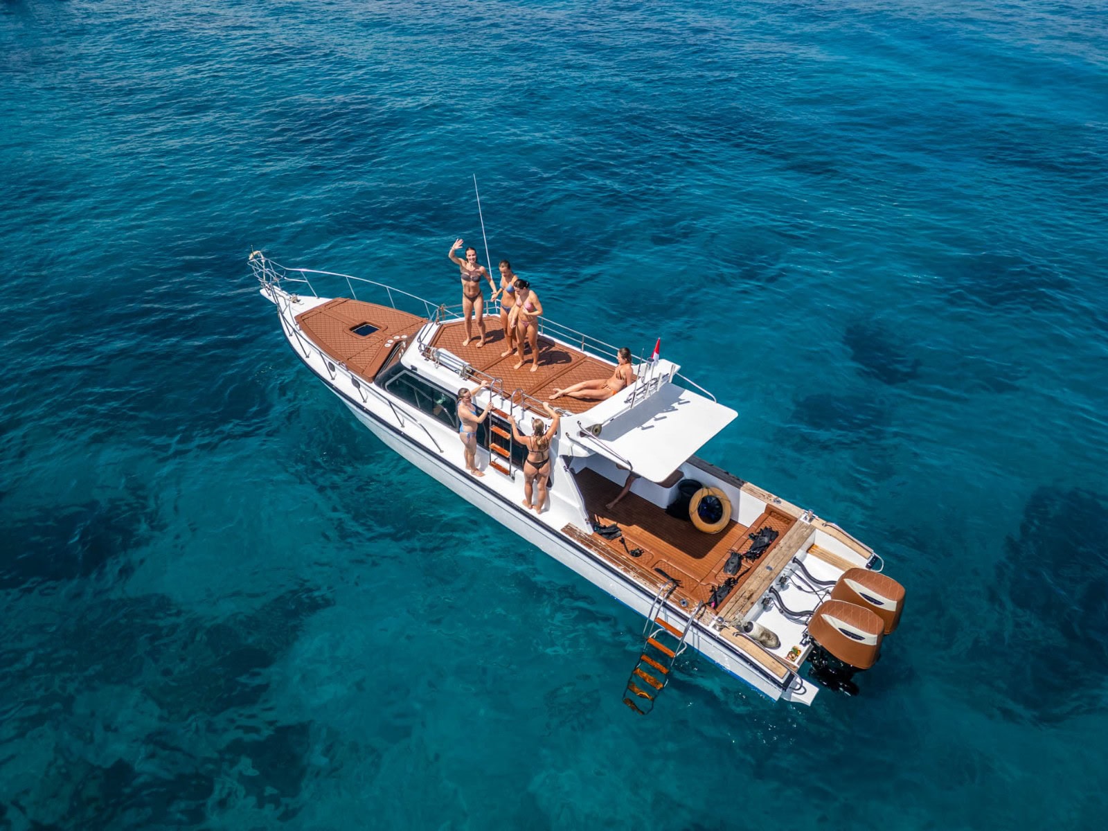 Luxury yacht with people practicing yoga and relaxing on deck in clear blue waters.