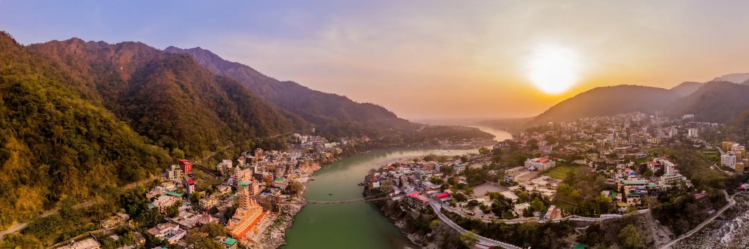 Scenic view of Rishikesh with river and mountains at sunset.