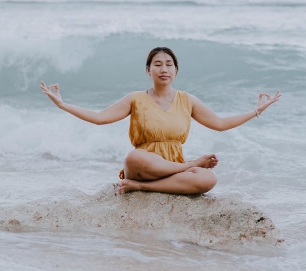 Woman meditating on a rock at the beach during sunset.